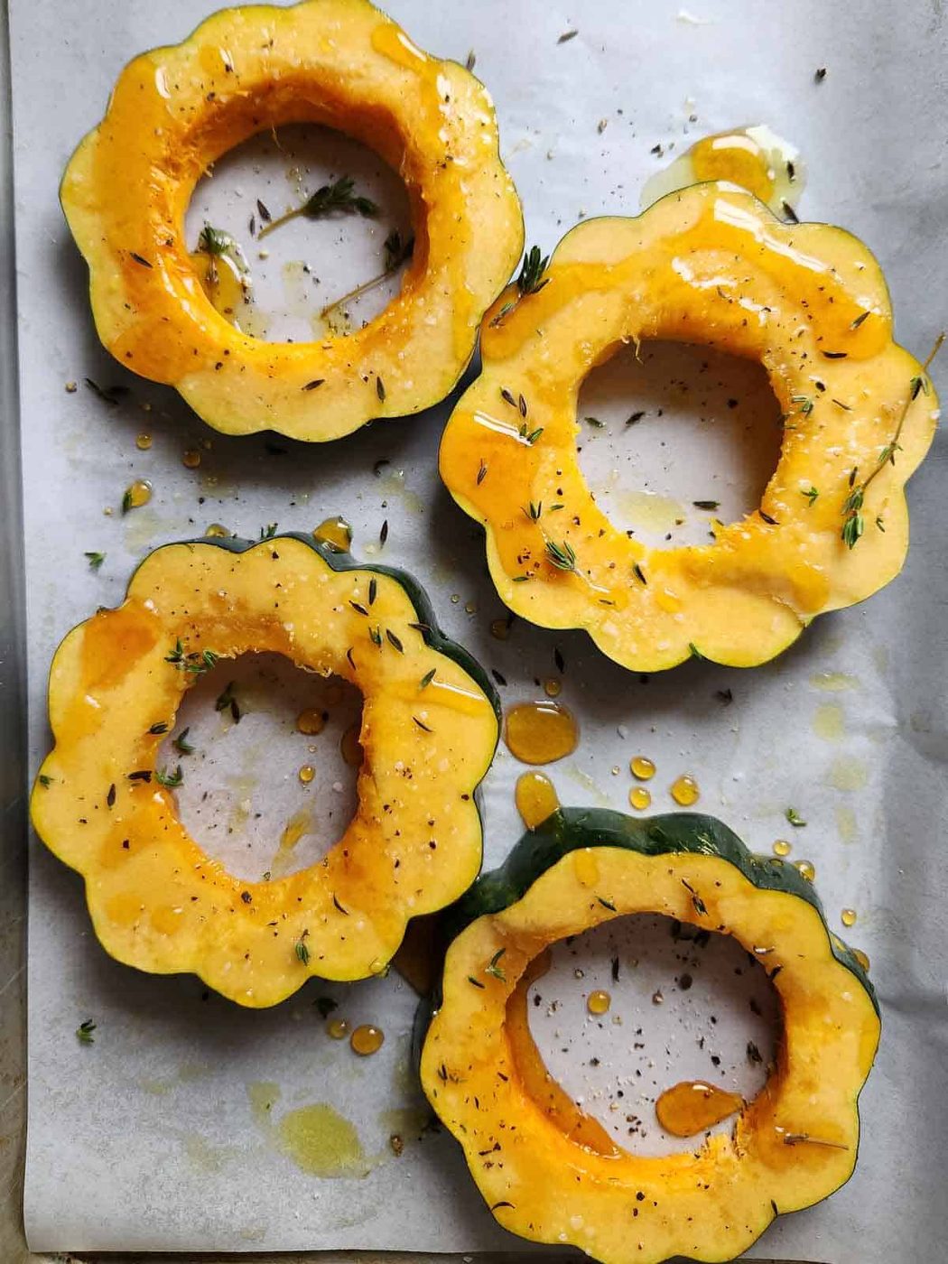 Four acorn squash rings drizzled with honey and seasonings on a baking sheet.