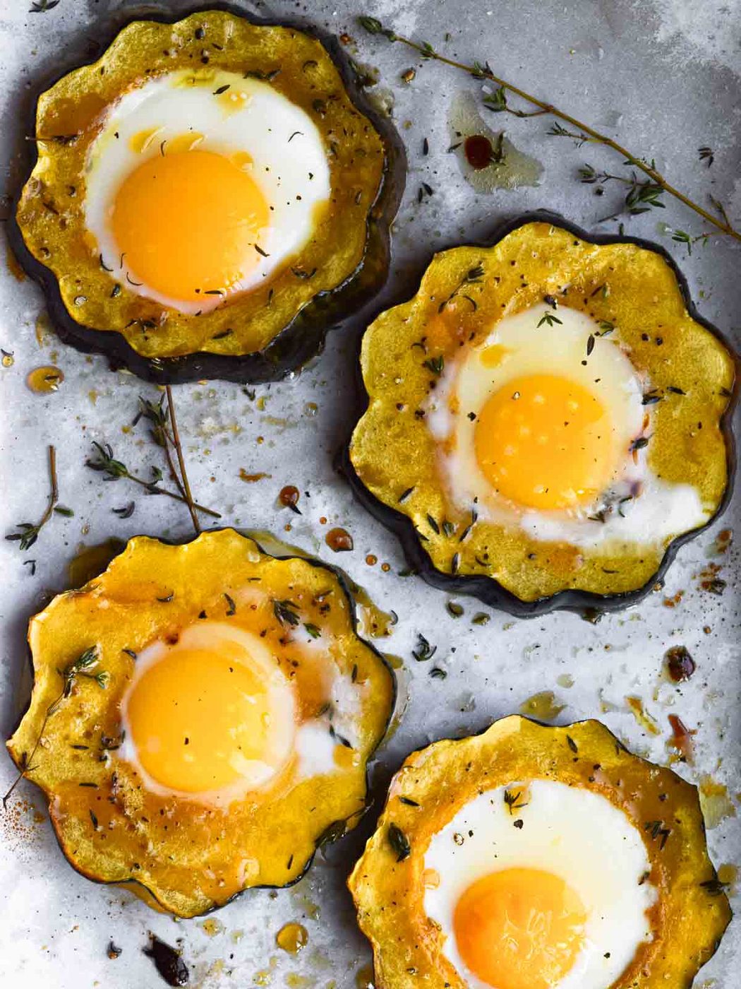 Overhead view of acorn squash egg in a hole with honey and thyme on parchment paper.