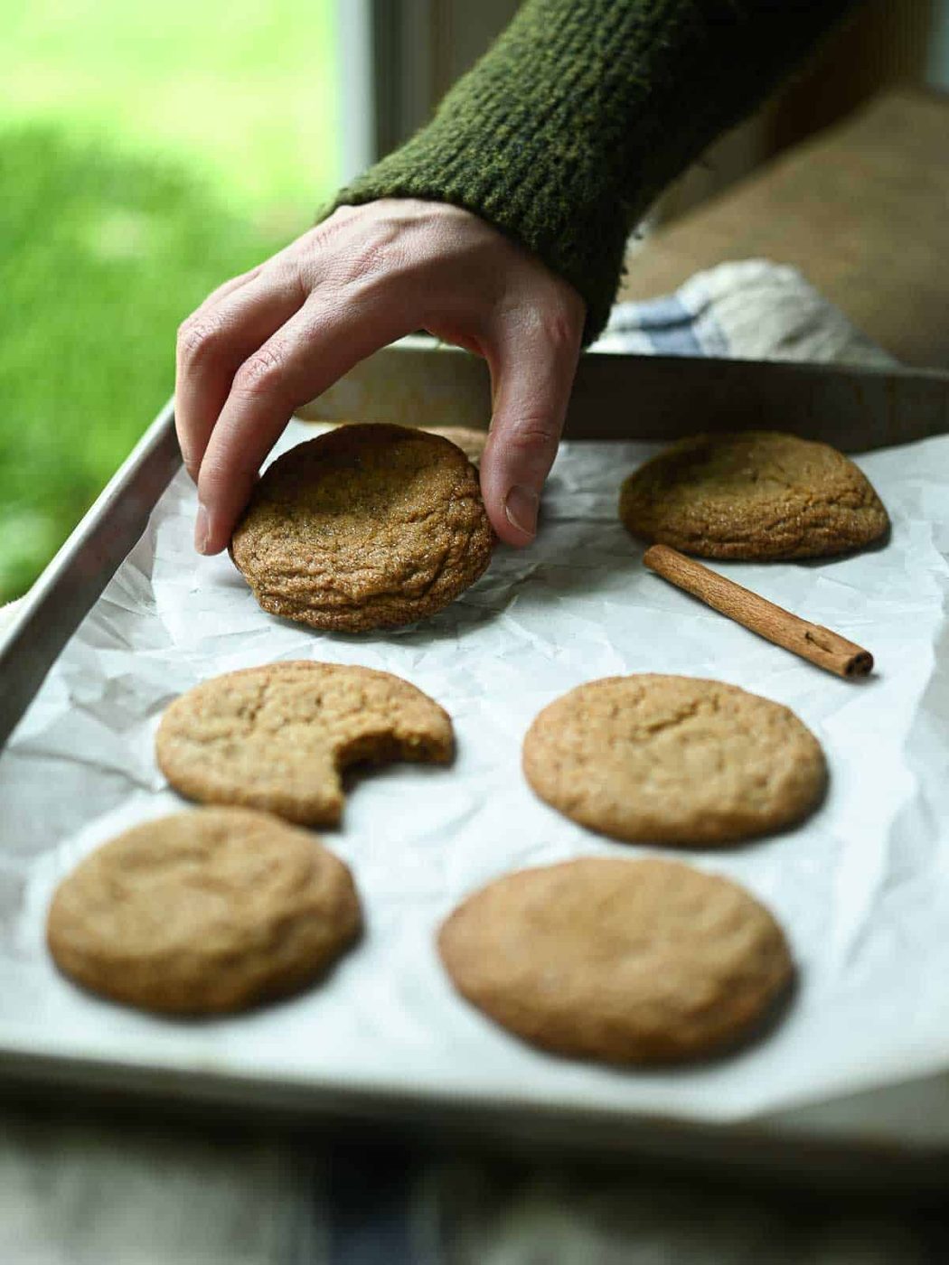 Hand grabbing for a cookie off a tray next to a window.