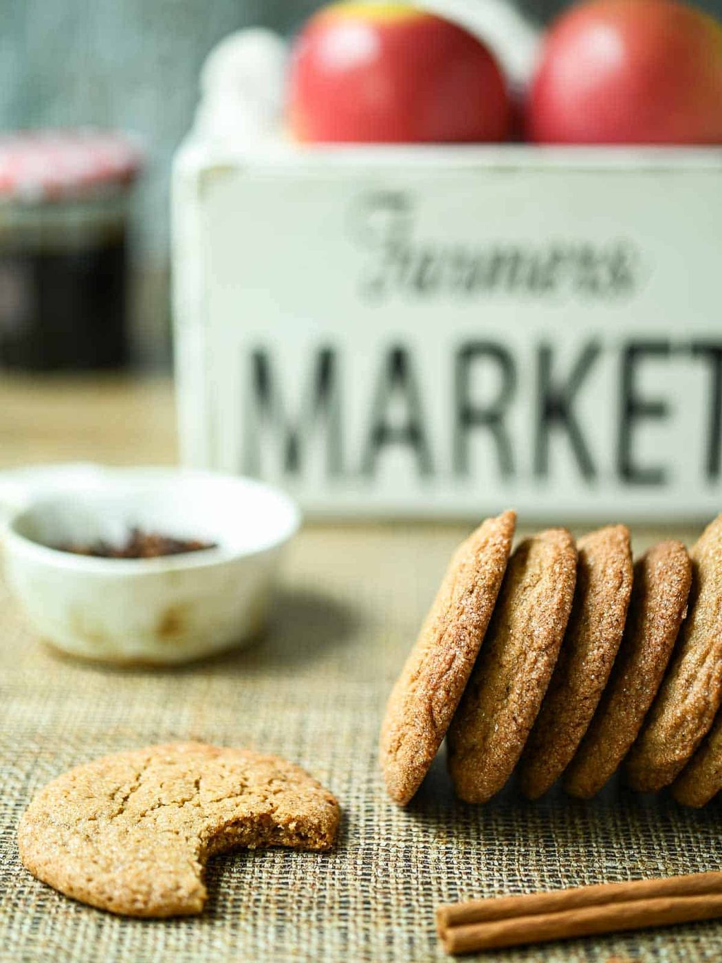 Side view of cider cookies on a brown surface with cinnamon and apples in the background.