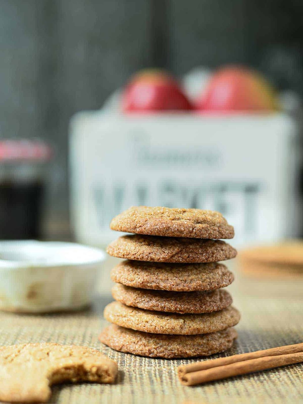 Eye level view of apple cider cookies stacked tall with a bucket of apples in the background.