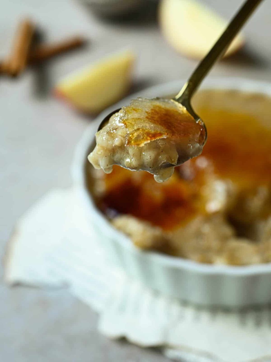 Oatmeal on a spoon with apples blurred in the background.