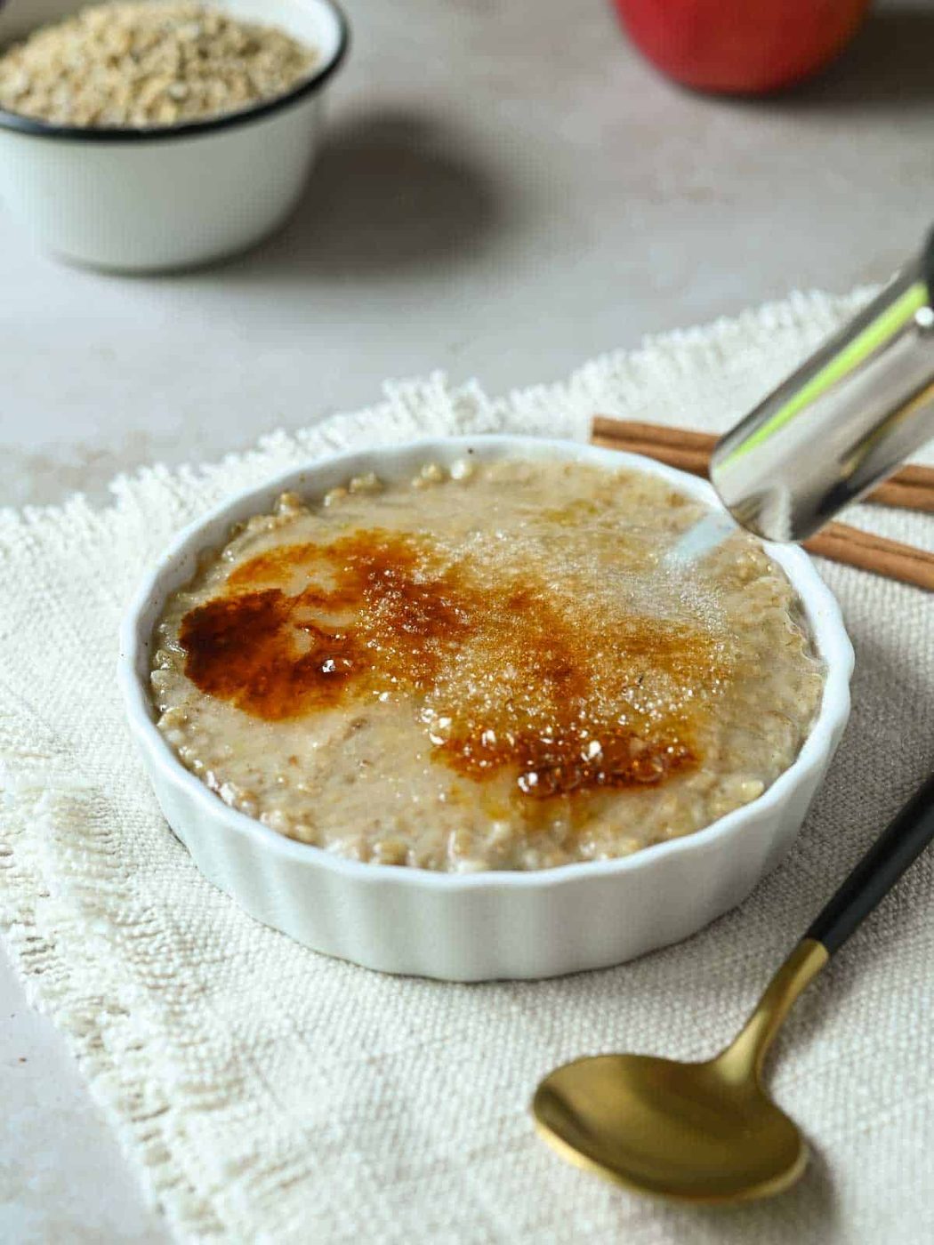 Top of oatmeal in a white dish being swept with a kitchen torch.