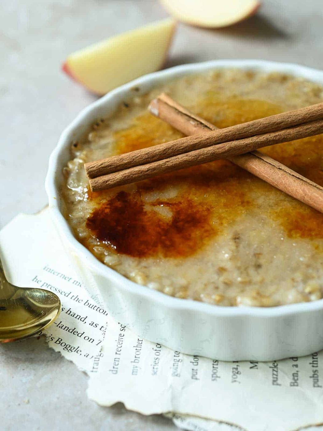 Apple oatmeal brulee in a white dish with cinnamon sticks on top.