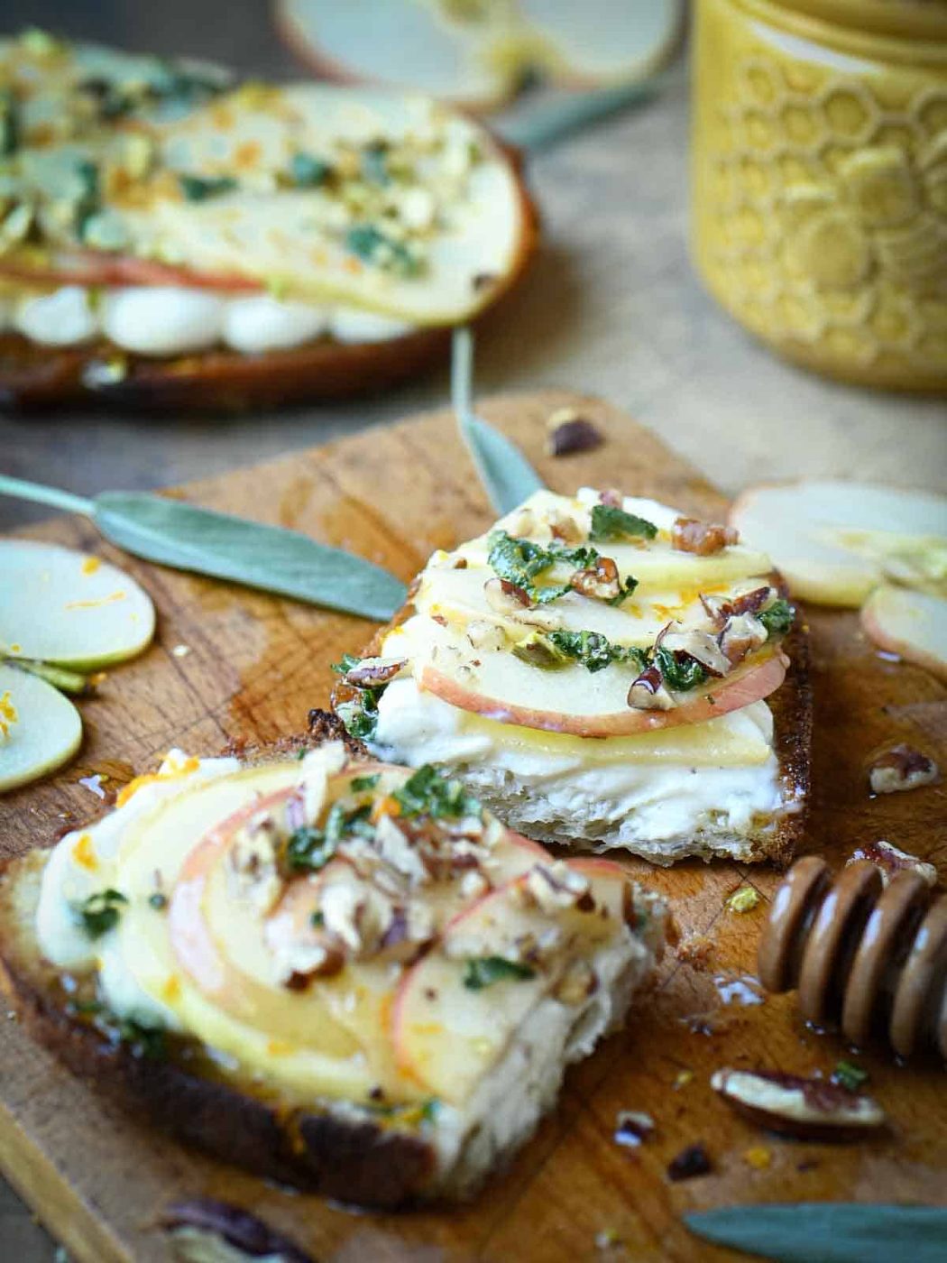 Apple toast sliced open on a cutting board with sage and honey.