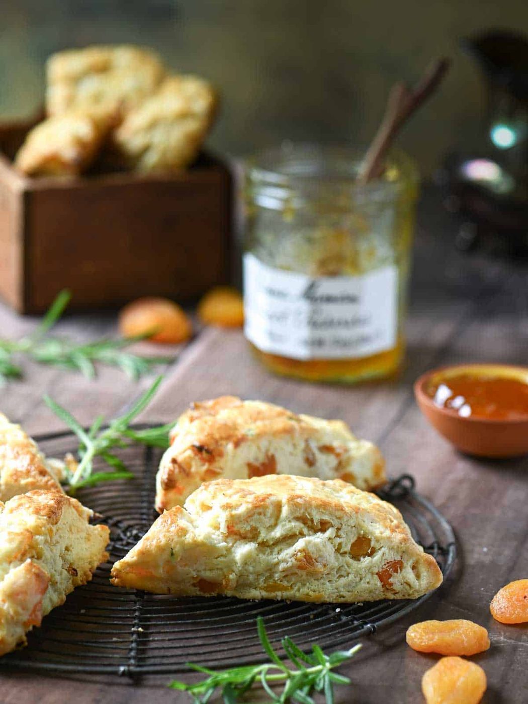 Scones on a wire rack with jam and apricots in the background.