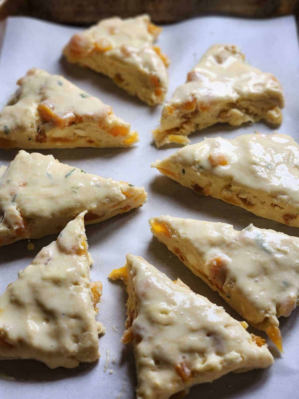 Scones on a baking sheet brushed with egg wash.