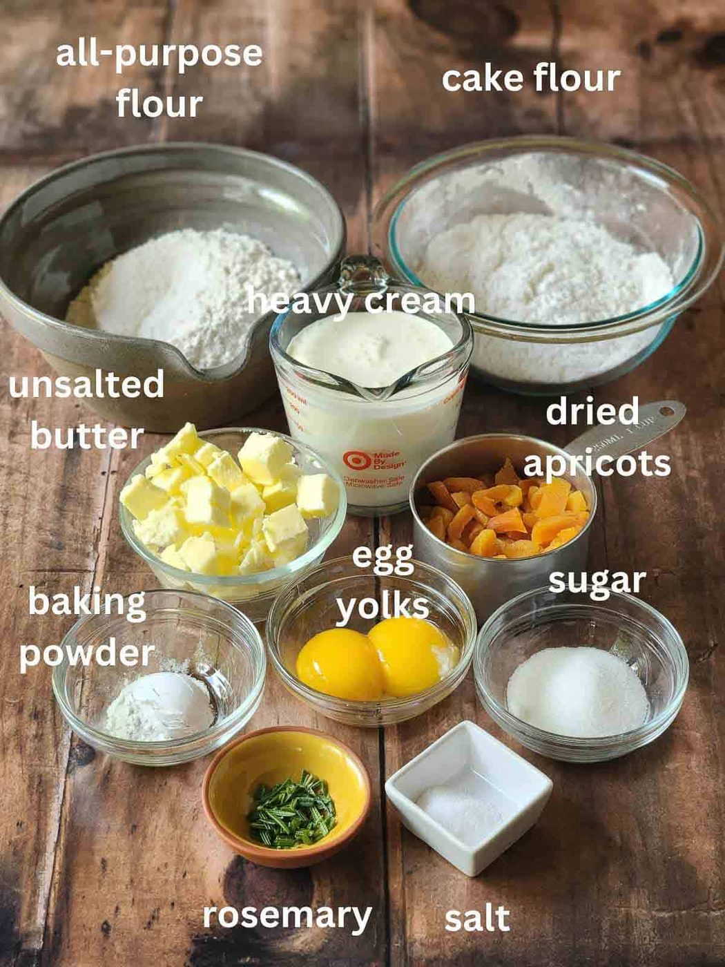 Ingredients for rosemary scones in bowls on a wood surface.