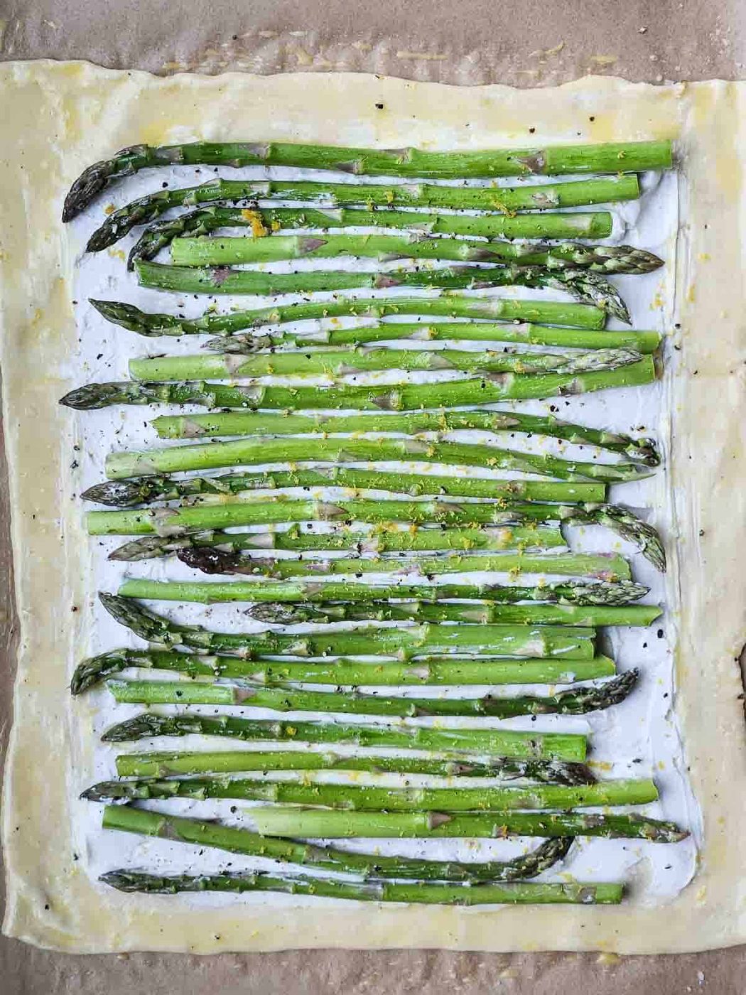 Uncooked puff pastry with goat cheese and asparagus on top.