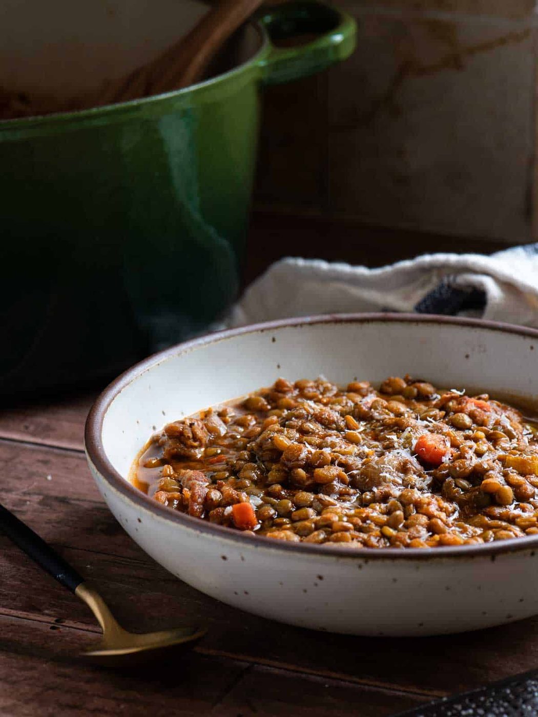 Lentil soup in a bowl, with a green pot in the background.