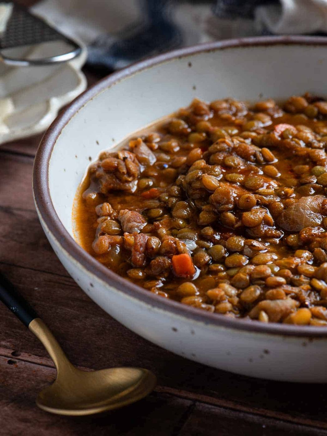 Bacon lentil soup in a bowl on a wood surface with a spoon.