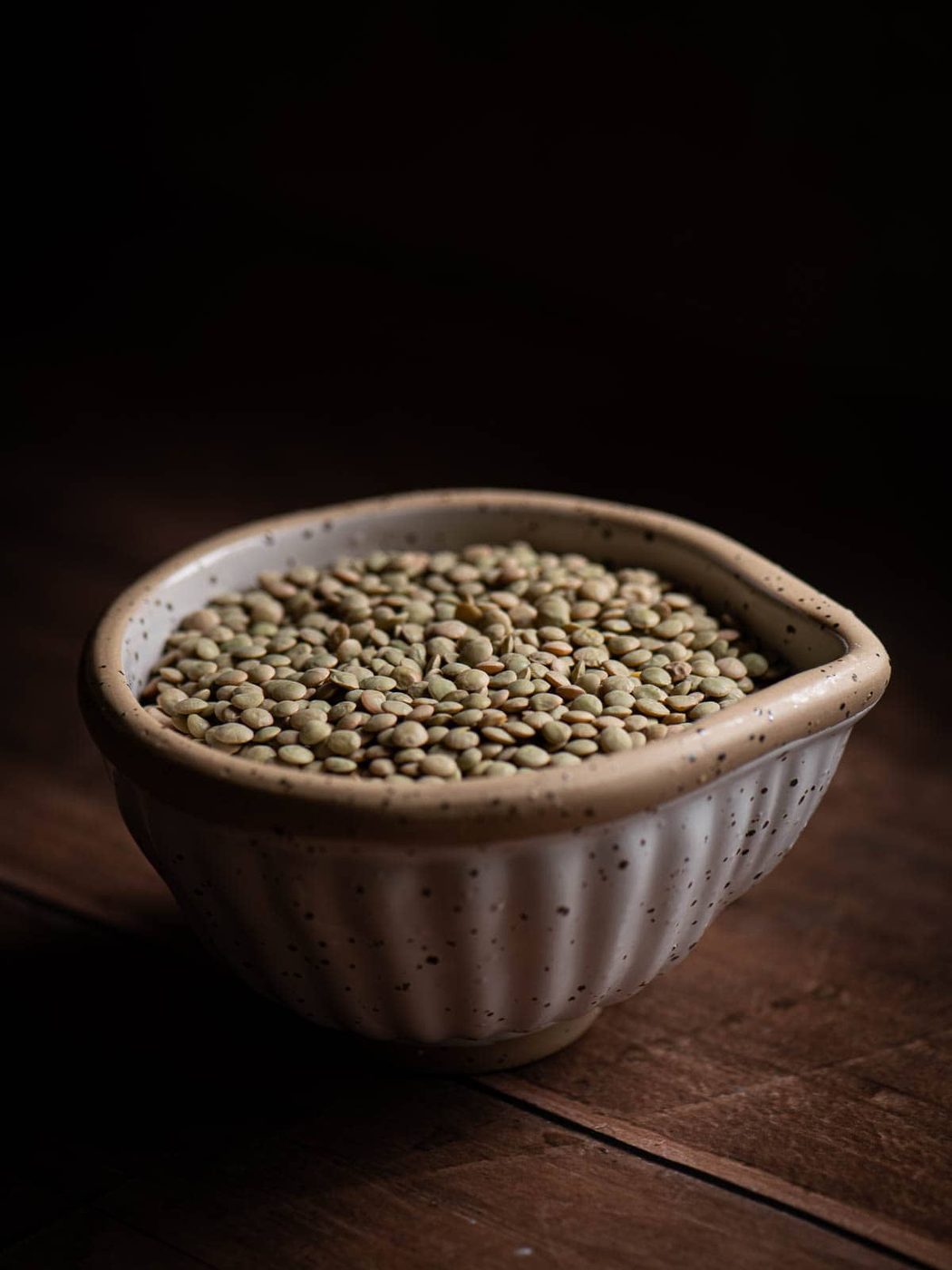 Dry green lentils in a beige bowl.