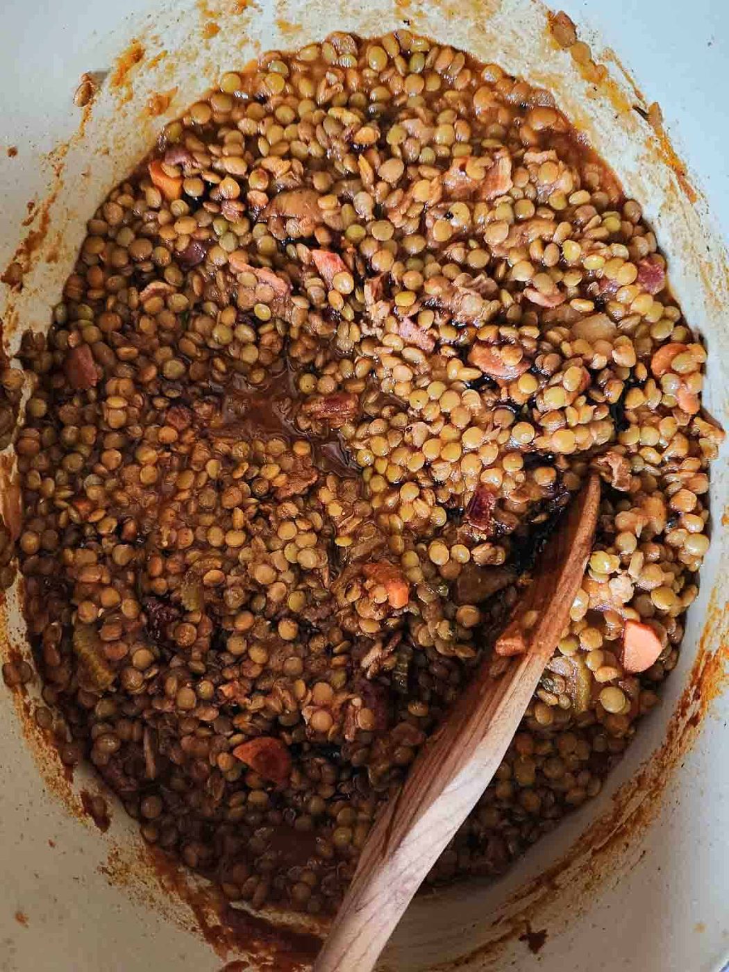 Overview of bacon lentil soup in a pot with a wooden spoon.