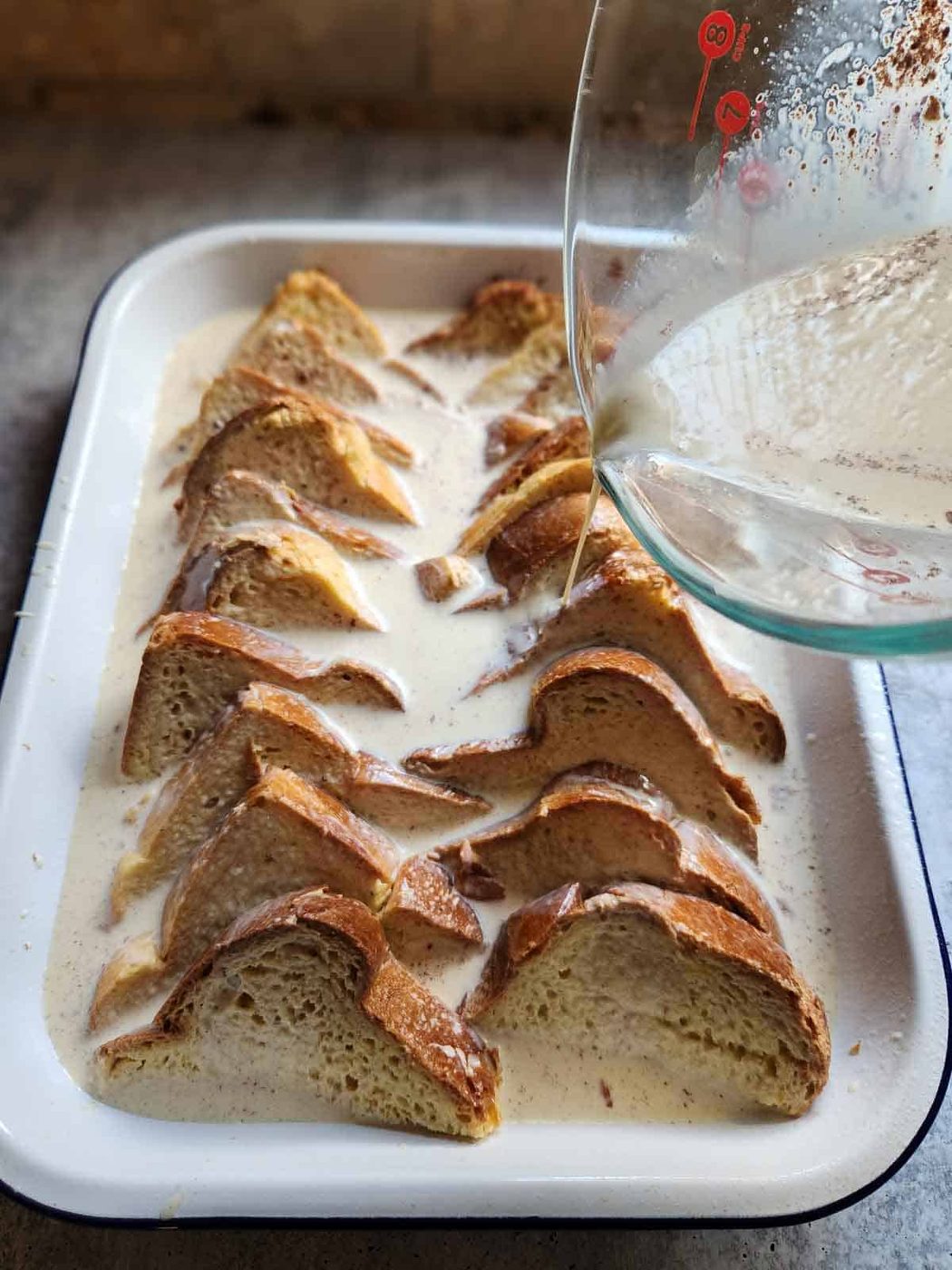 Custard being poured over bread for Baked Brioche French Toast.