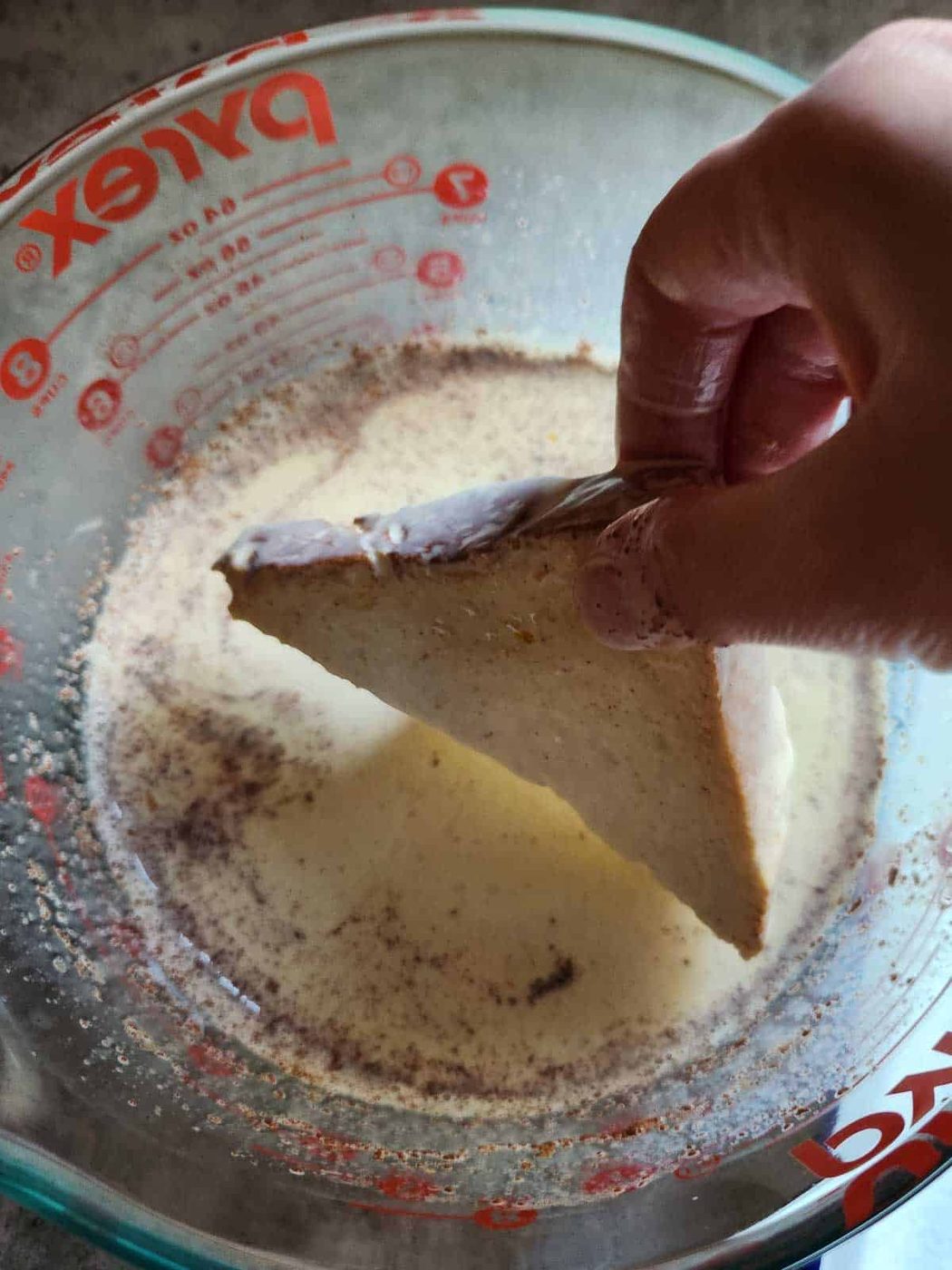 Slice of bread being dipped into French toast batter.