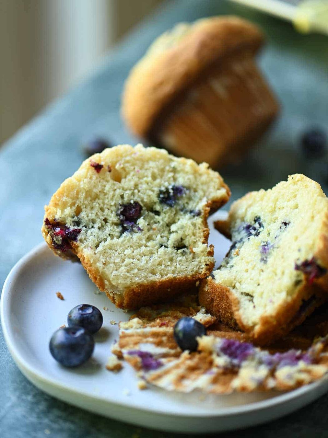 A blueberry muffin sliced in half, showing the texture on a white plate.
