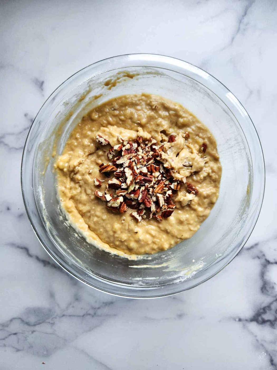 Pecans added to banana bread batter in a bowl.