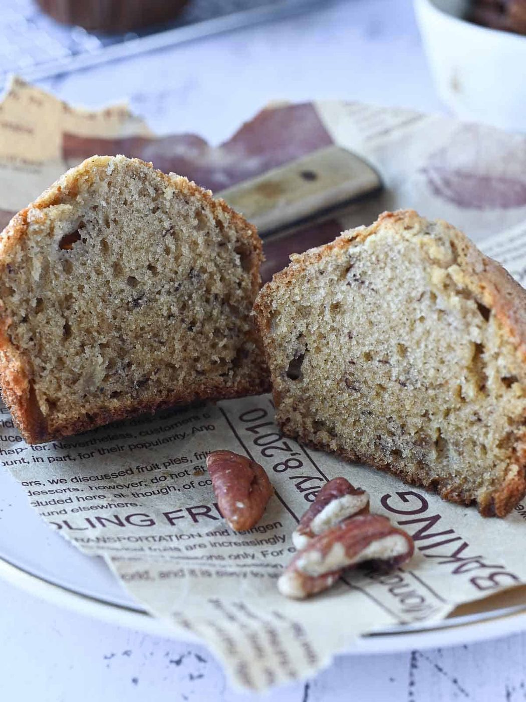 Banana pecan muffins cut in half on a plate with pecans in the front.
