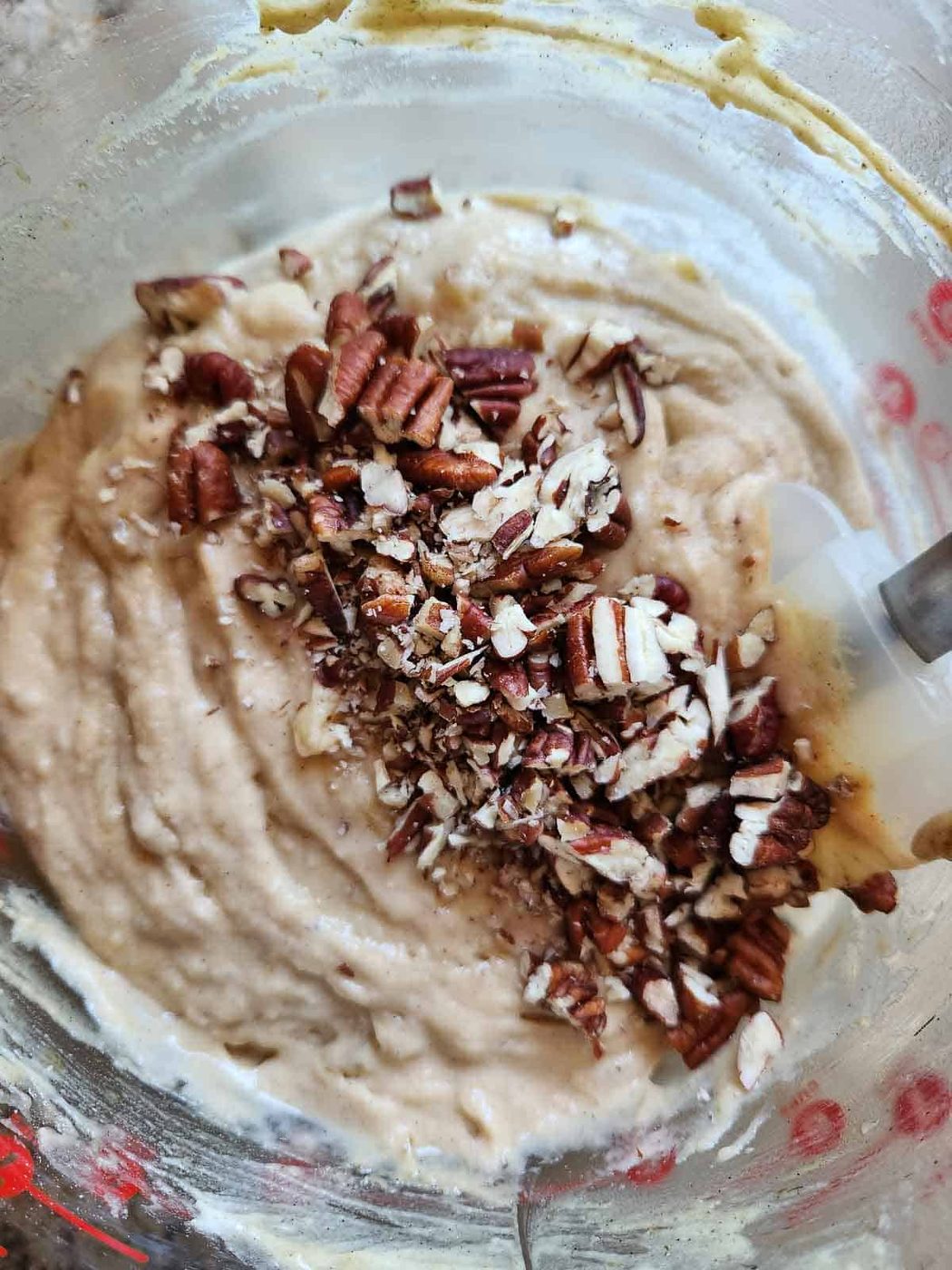 Banana muffin batter with pecans in a clear bowl.