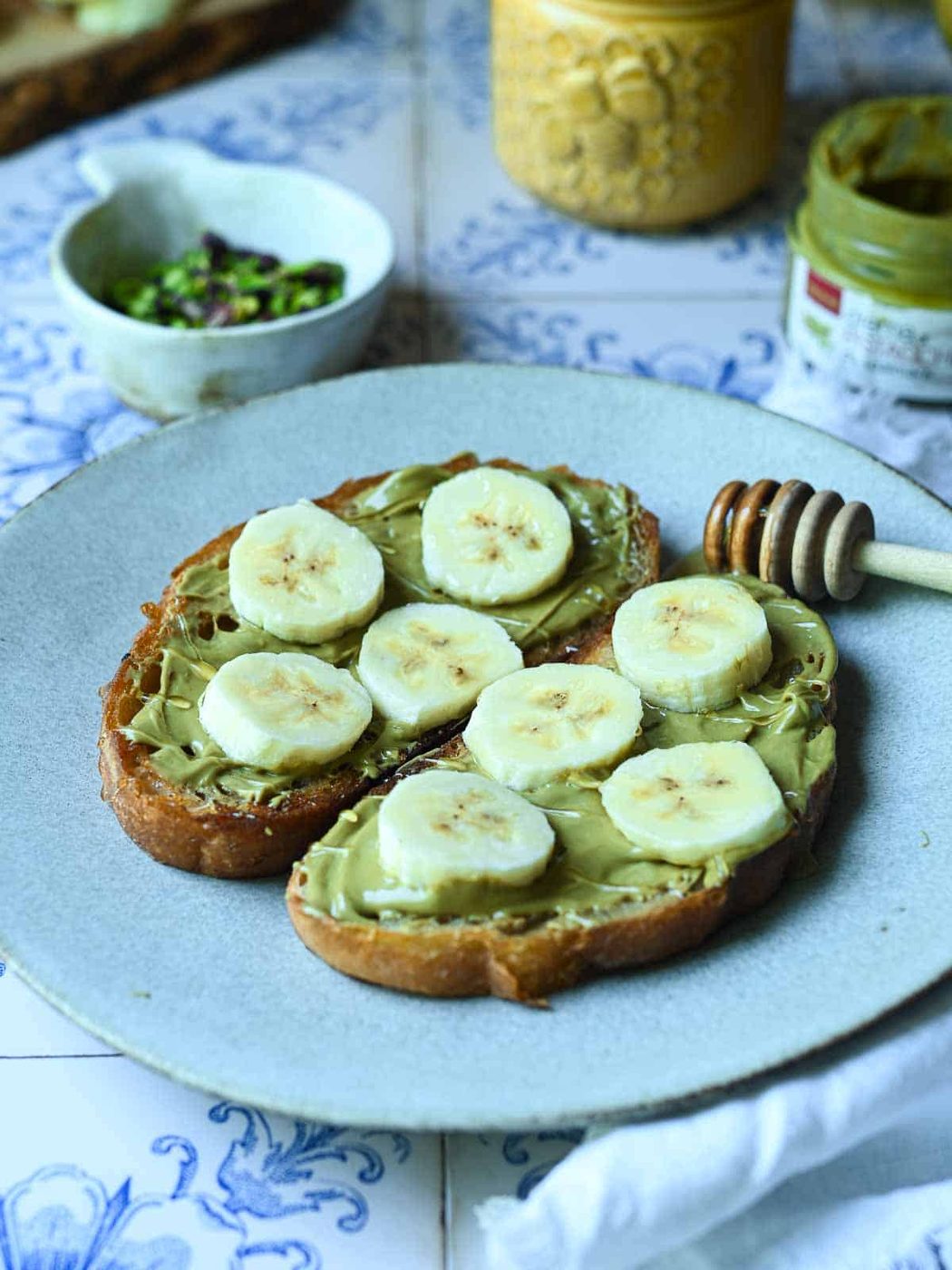 Sliced bananas and pistachios on toast with honey spread on a white plate.