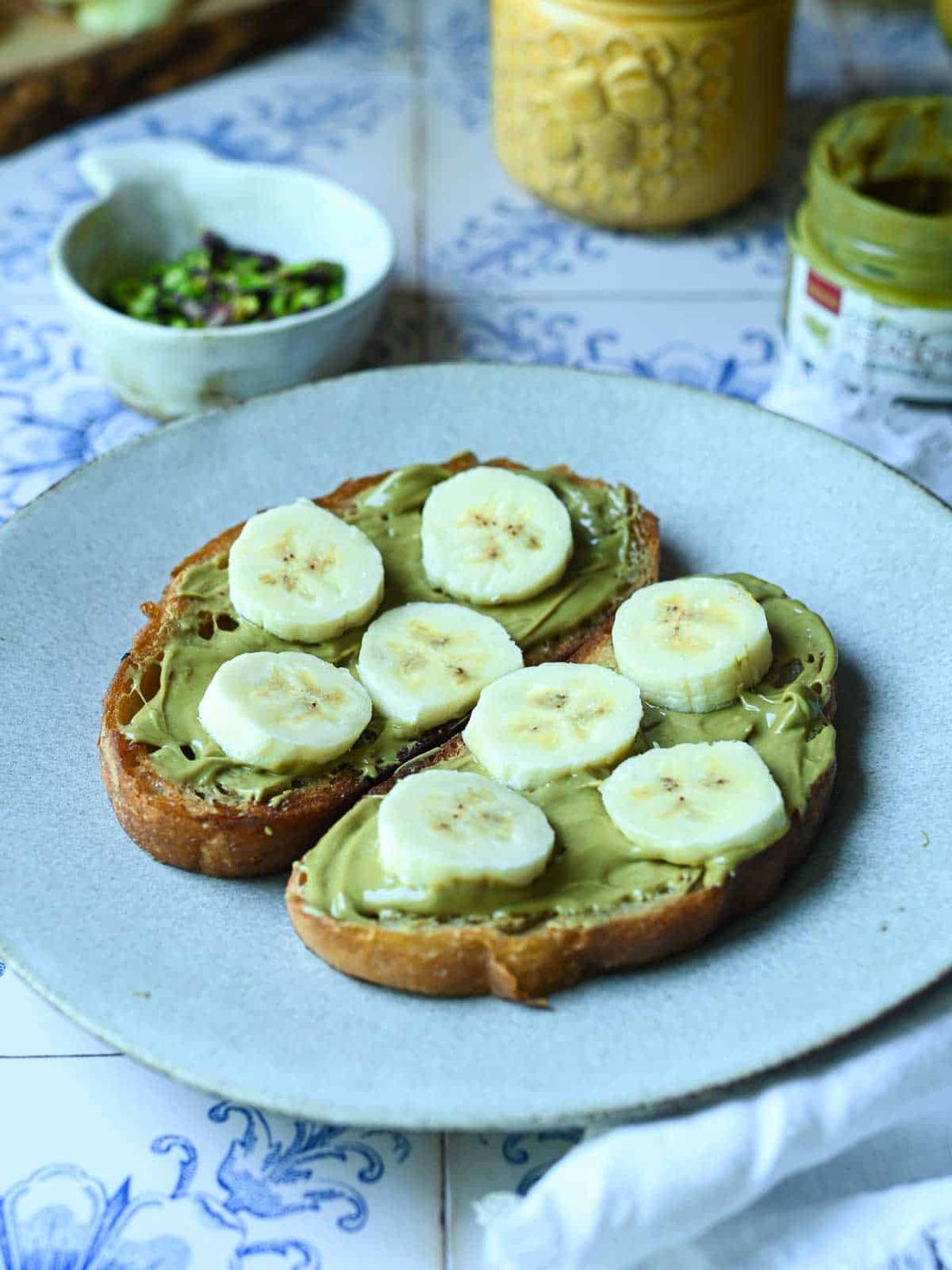 Sliced bananas on toast with pistachios on top of a white plate.