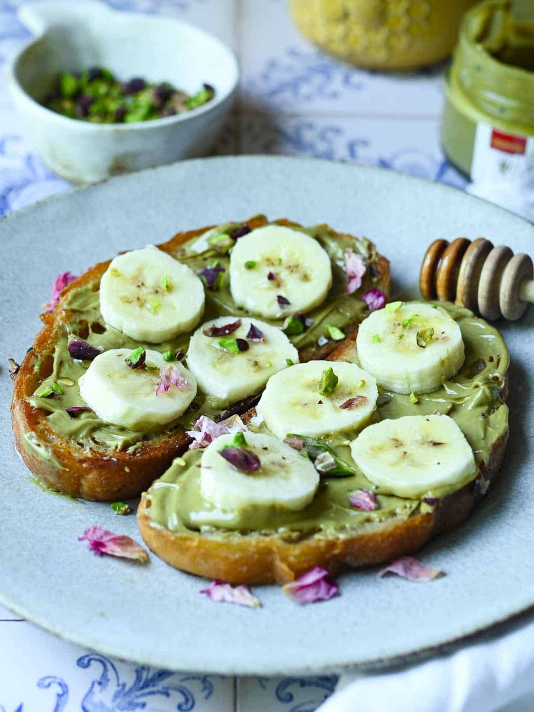 Banana and pistachio toast on a white plate with honey in the background.