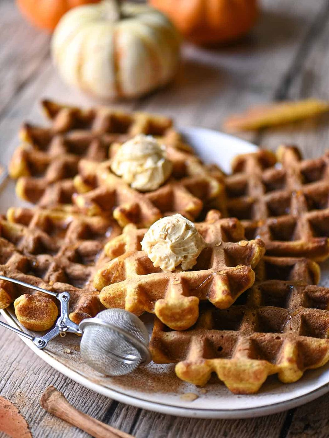 Pumpkin waffles on a platter with mounds of butter and cinnamon.