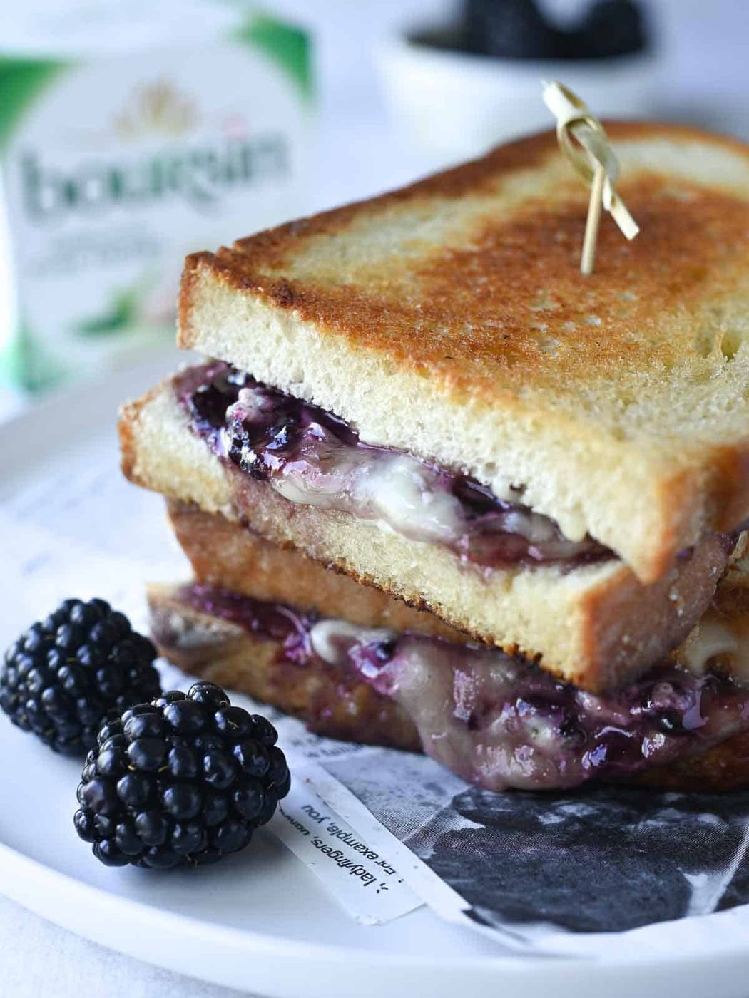 Blackberry boursin grilled cheese on a white plate with blackberries in the foreground.