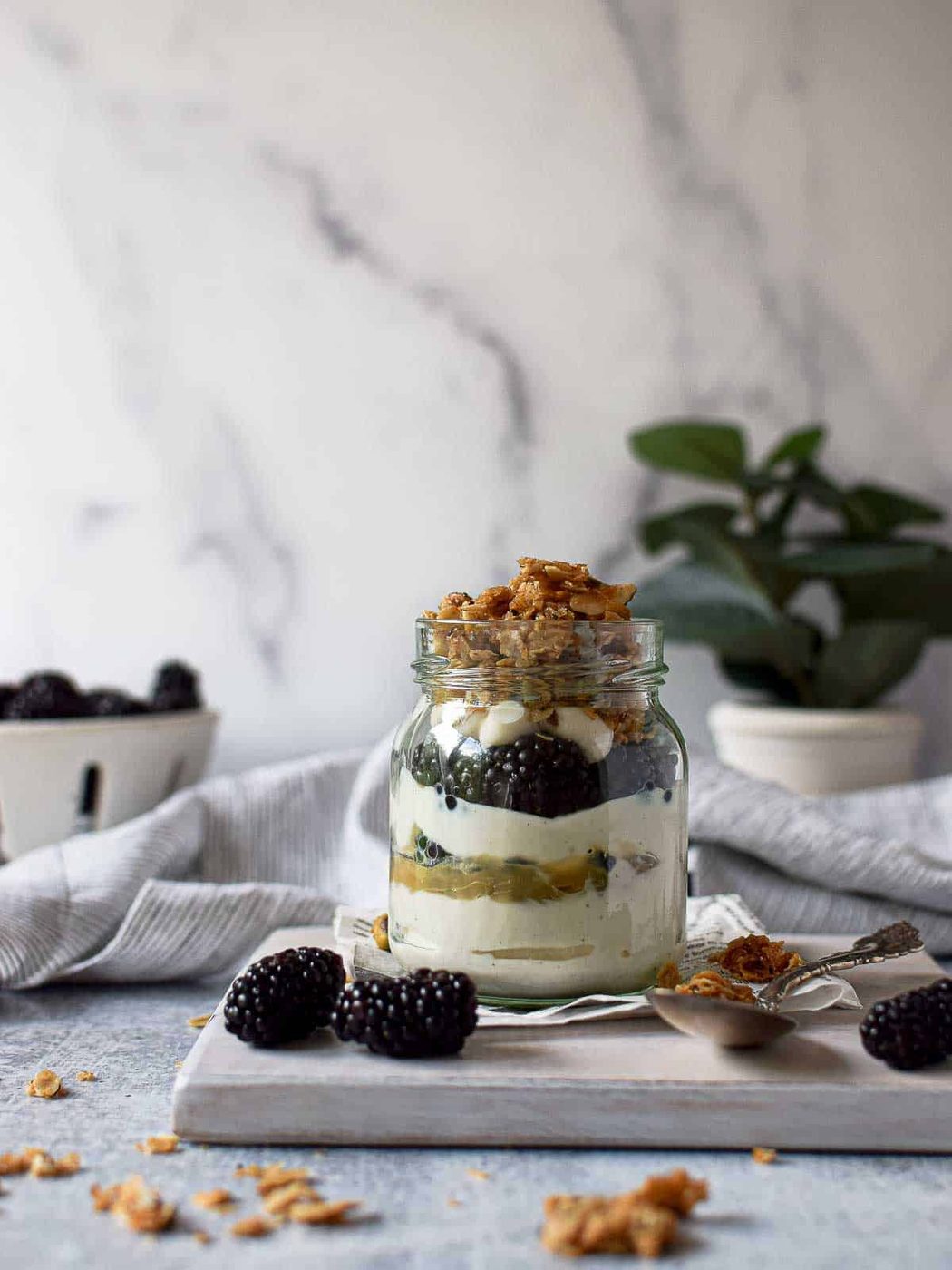 Eye level view of parfait in a jar layered with yogurt, blackberries lemon curd and granola on a grey background.