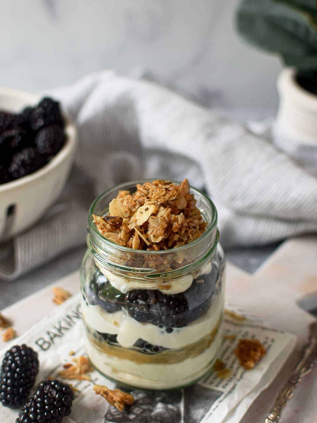 Angled view of yogurt parfait with blackberries on a grey wooden board with blackberries in the background.