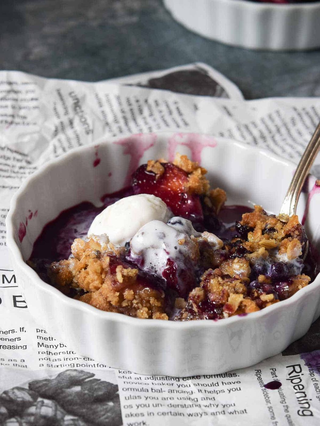 Small white dish of blueberry crisp with ice cream.