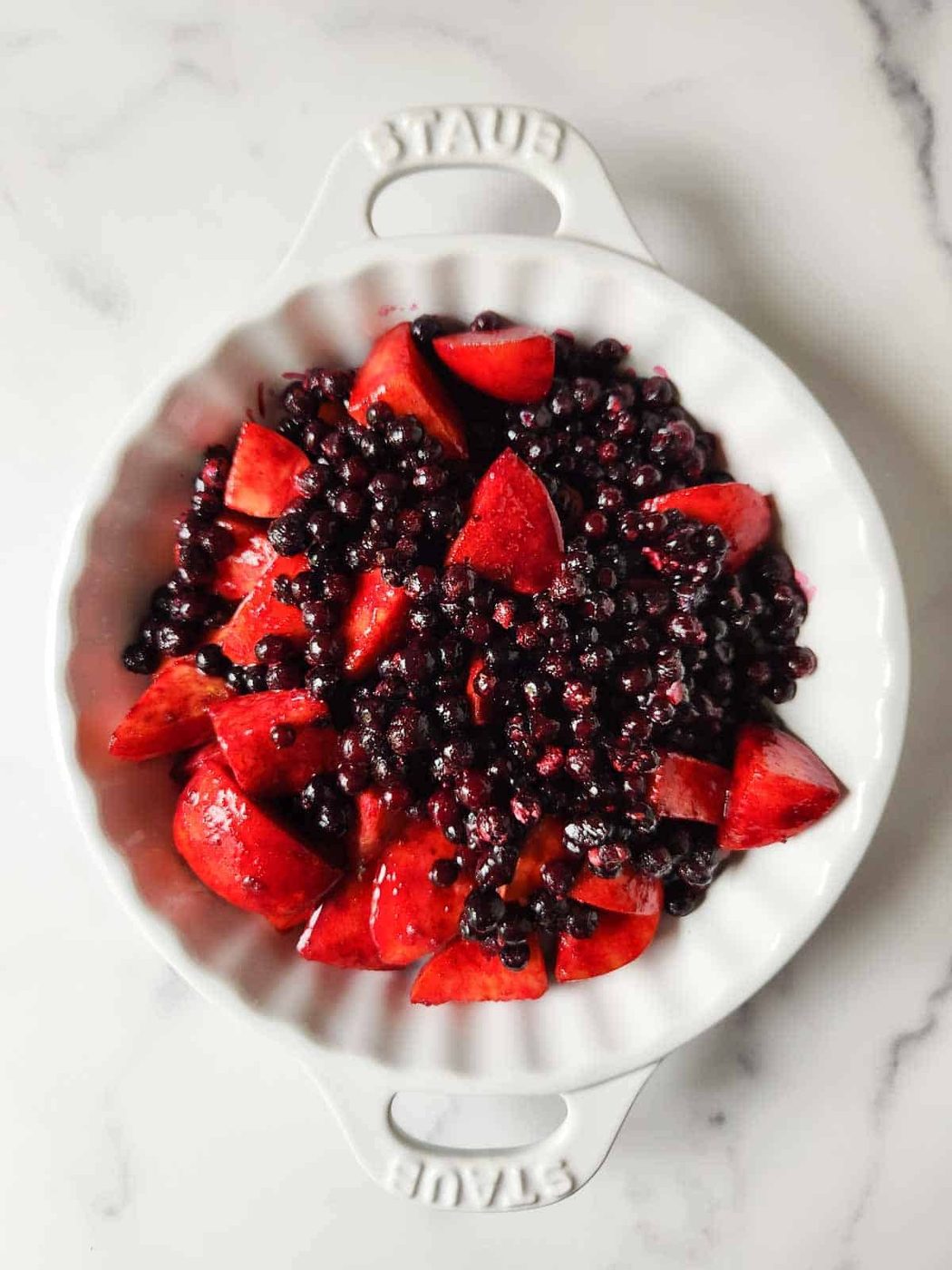 Blueberries and peaches in a white baking dish.