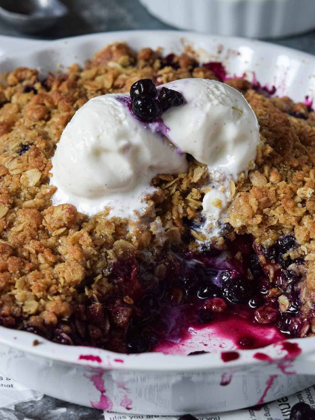 Close-up of peach blueberry crisp in a white pie plate with ice cream on top.