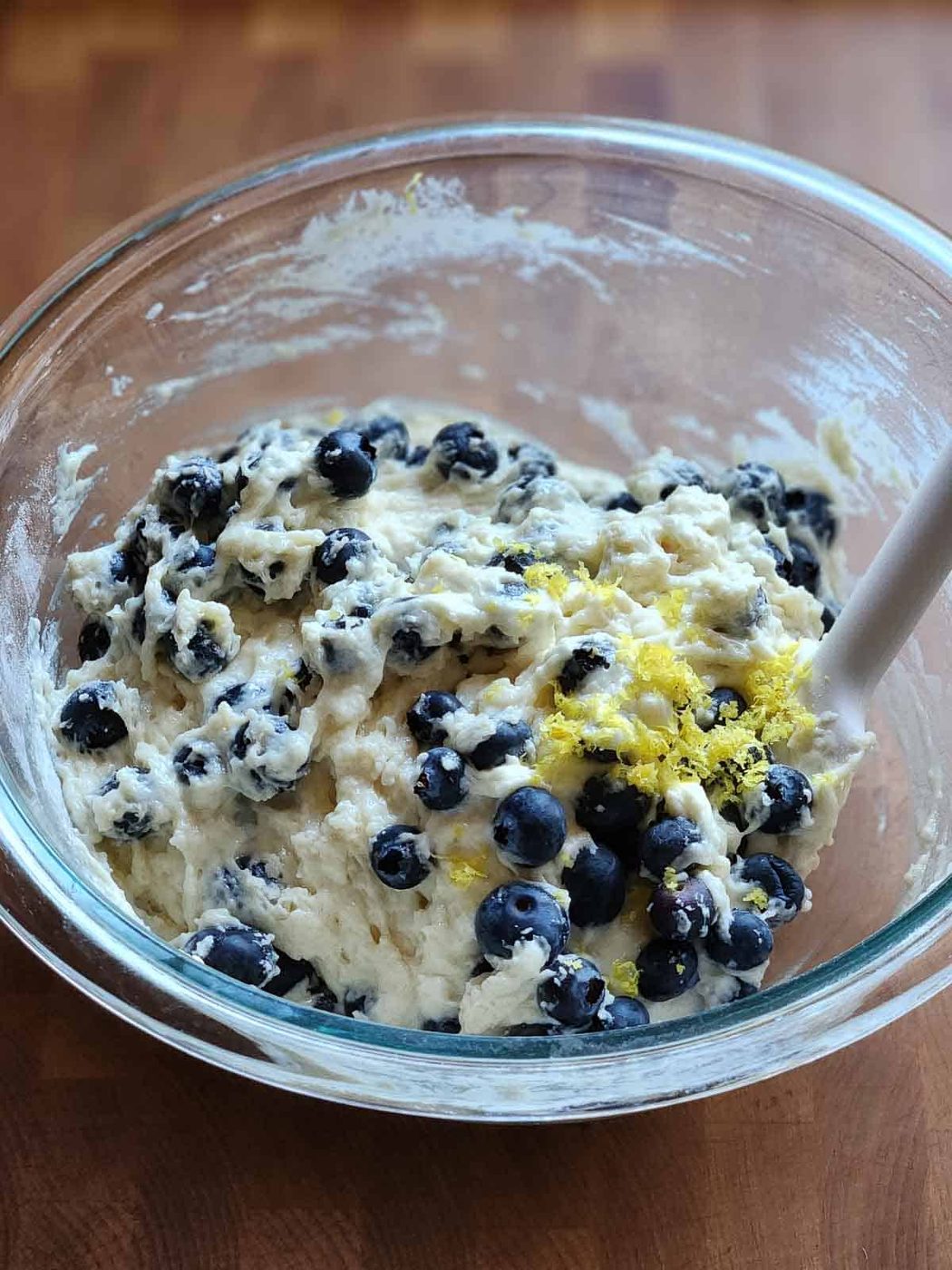 Blueberry pancake batter in a clear bowl with a spatula.