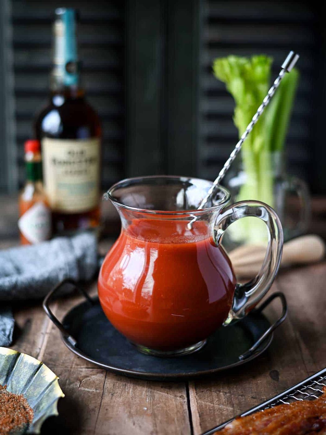 A clear pitcher of bloody mary mix on a wood surface.
