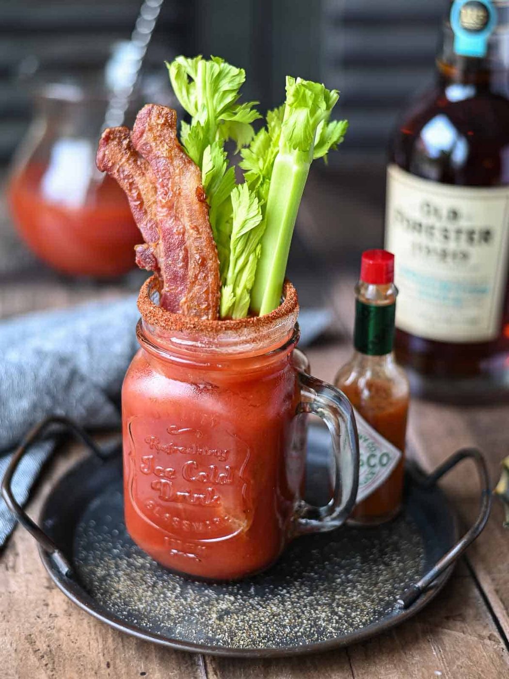 Angled view of a bacon bloody mary in a clear Mason jar on a metal tray.