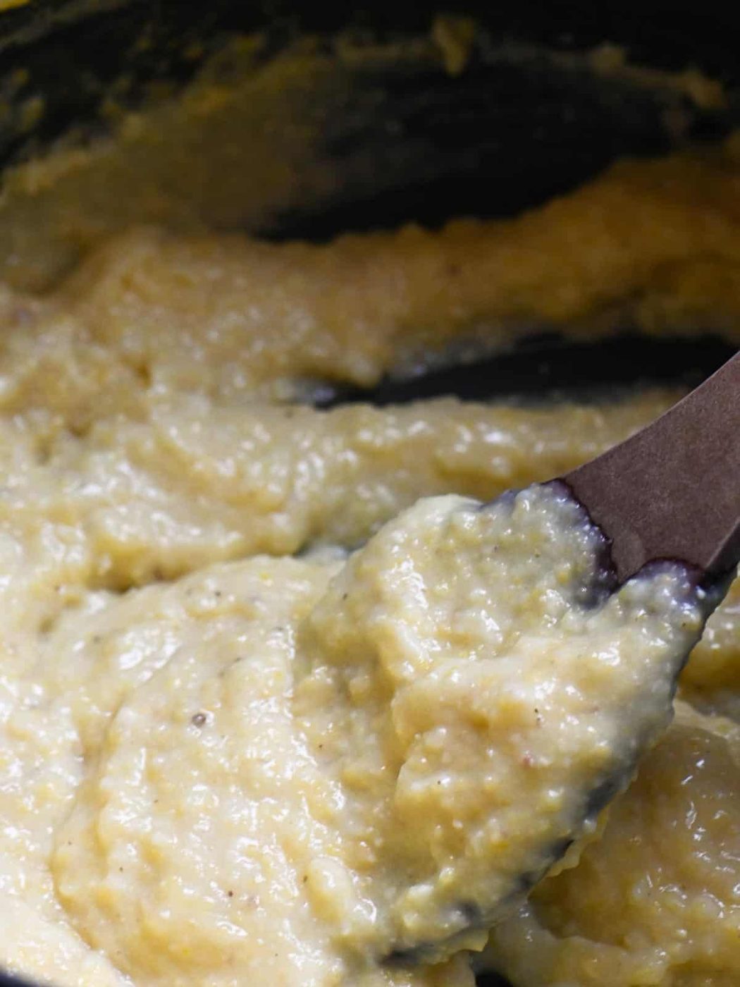 Creamy polenta being stirred with a wooden spoon in a pot.