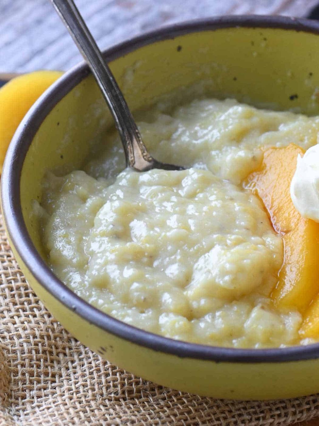 An angled view of creamy polenta in a yellow bowl with a spoon.