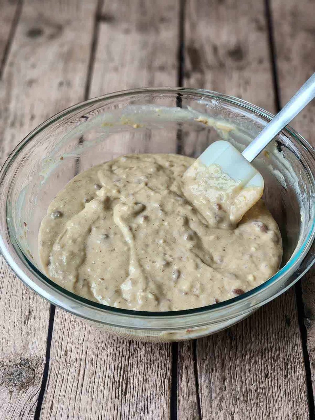 The batter for brown sugar date muffins in a clear bowl with a spatula.