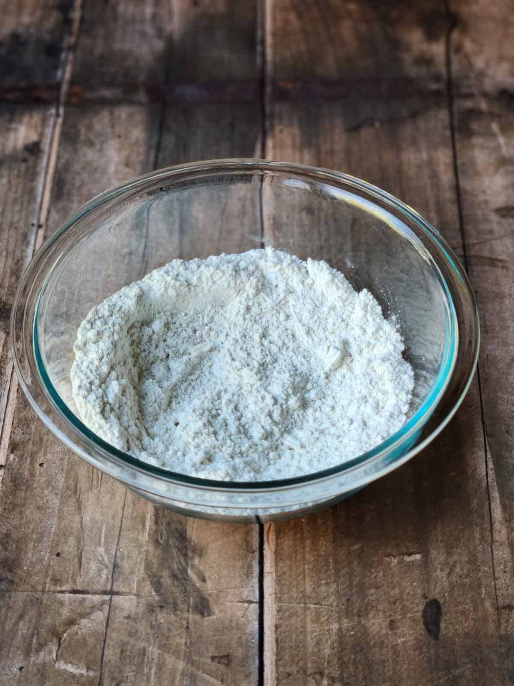 Dry ingredients in a clear bowl on a wood surface.