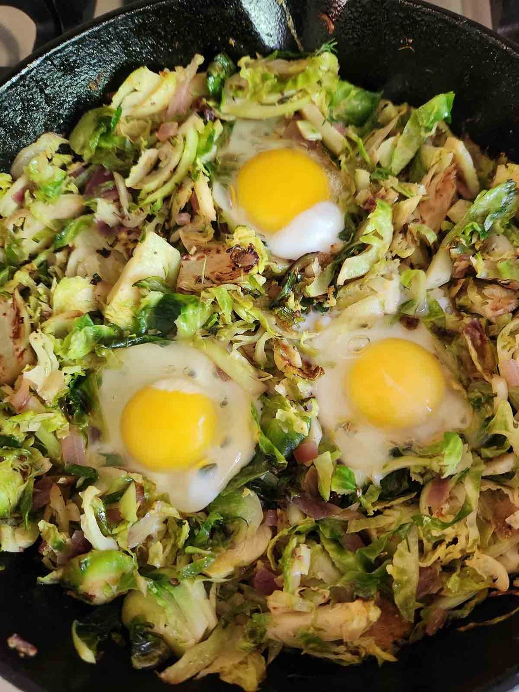 Brussel sprouts in a black skillet with 3 eggs in it.