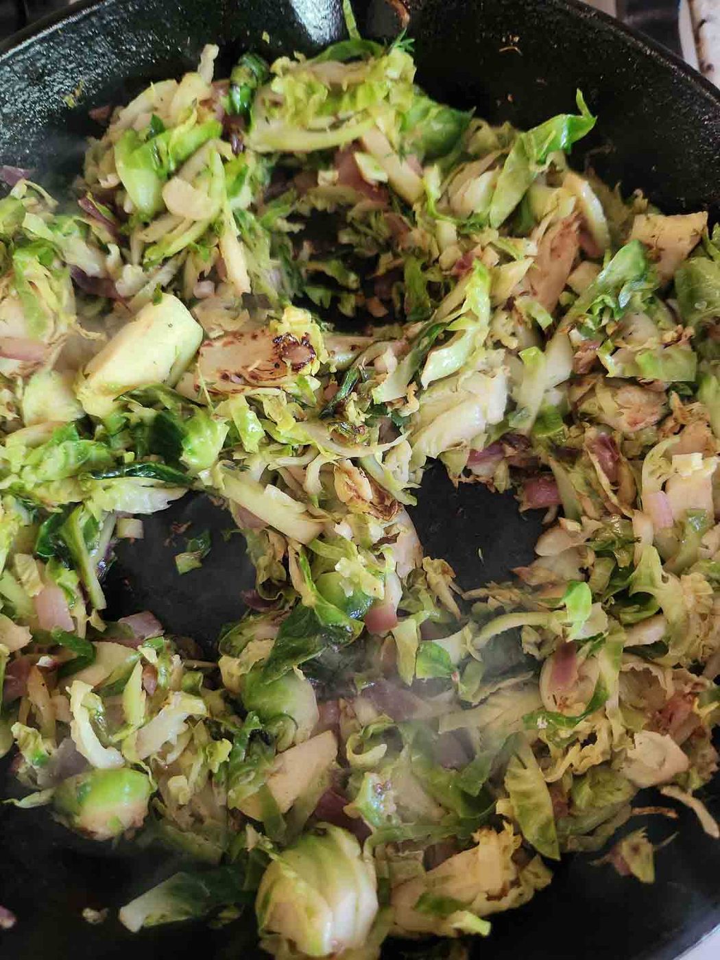 Brussel sprout hash in a skillet with 3 holes in it for eggs.