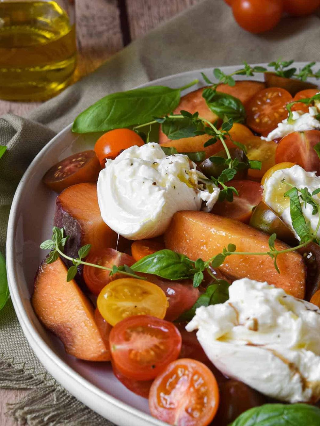 Close-up of burrata, peach, and tomato salad on a plate.