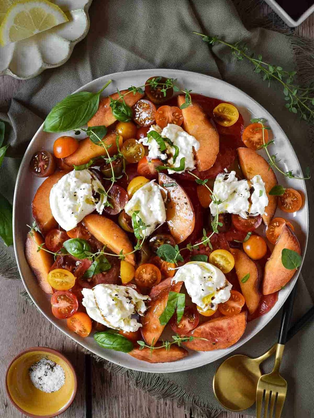 Overhead view of peach, tomato, and burrata salad on a white plate over a wooden surface.
