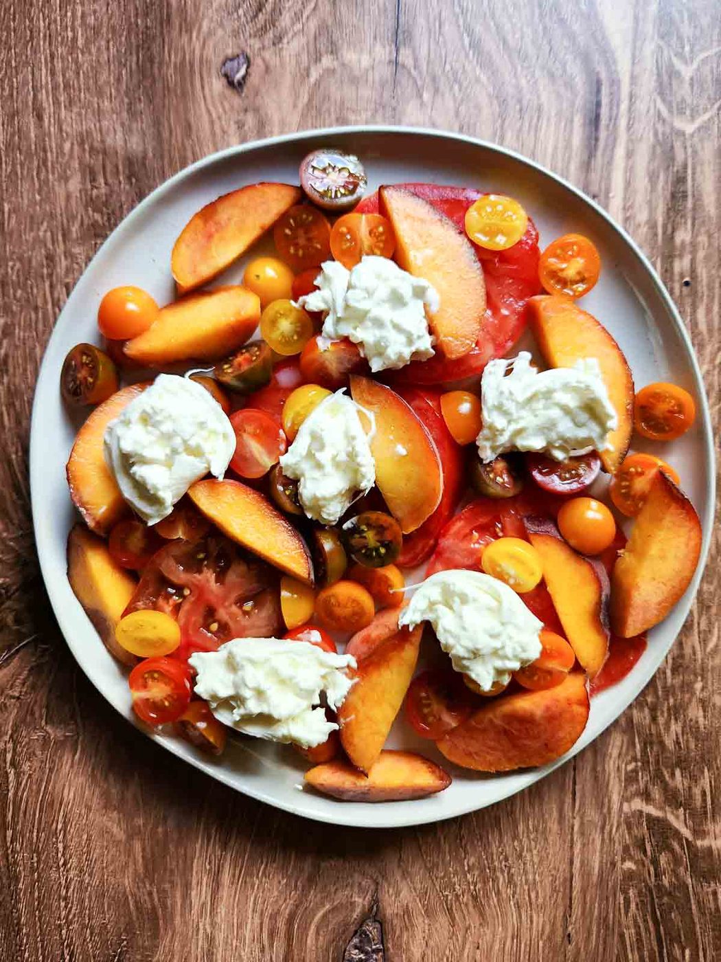 Tomatoes, peaches and burrata on a round plate.