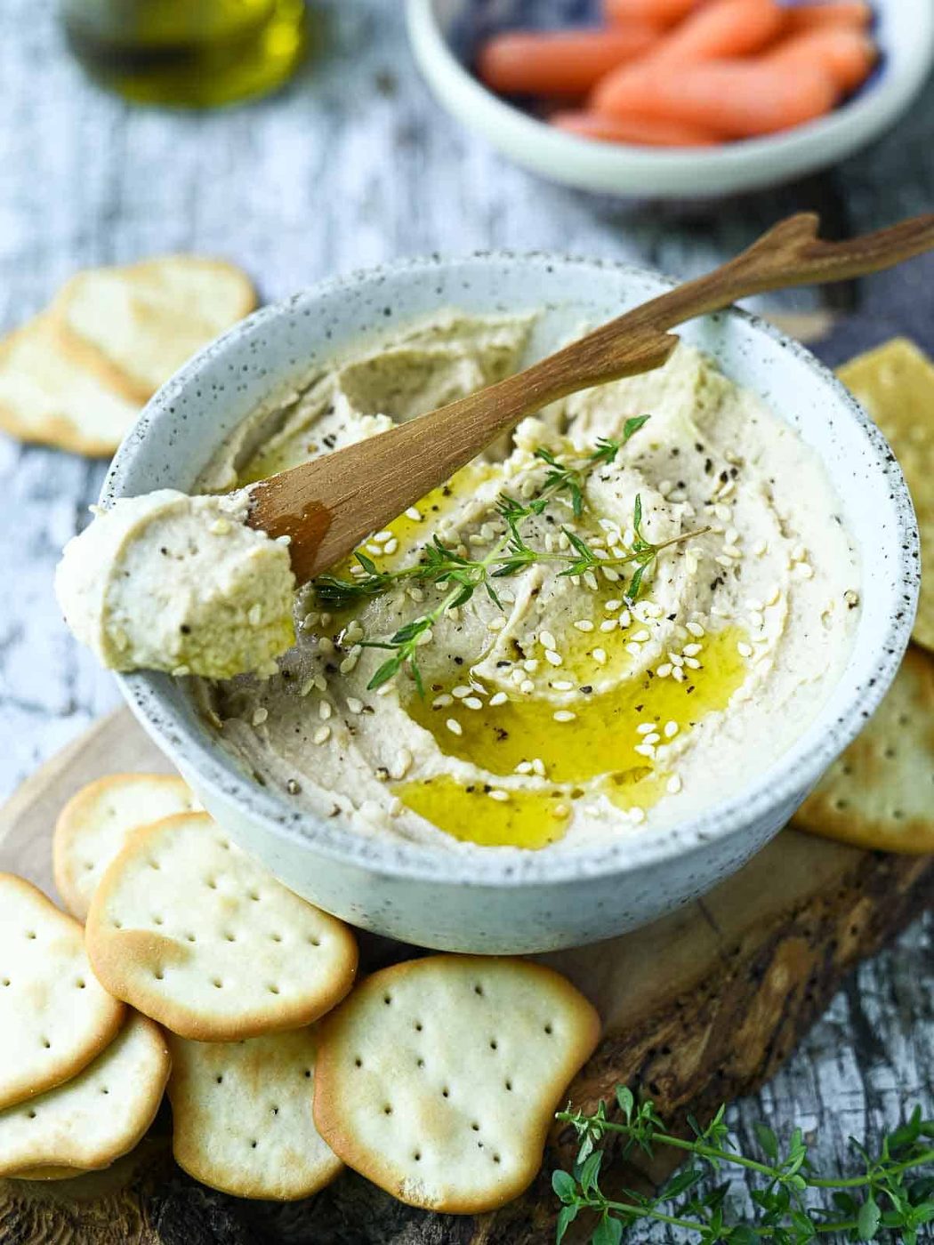 Hummus with a wooden spreader in a white bowl on a blue surface.