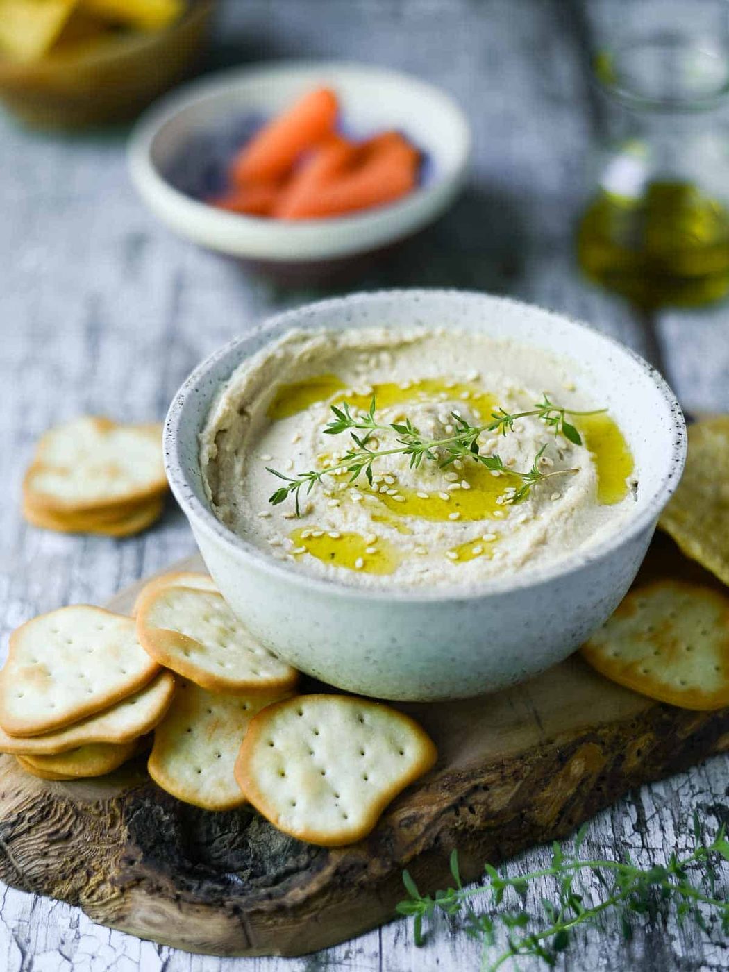 Butter bean hummus in a white bowl, with crackers around it.