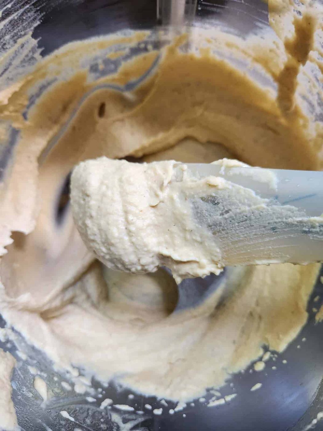 Blended butter bean hummus in a food processor with a spatula showing the consistency.