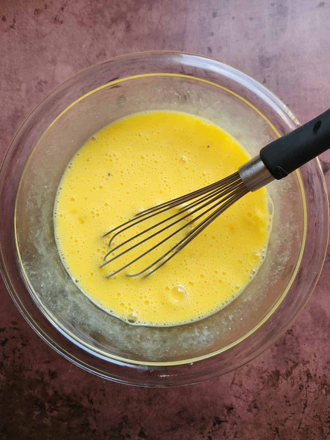 Scrambled egg mixture in a clear bowl with a whisk.