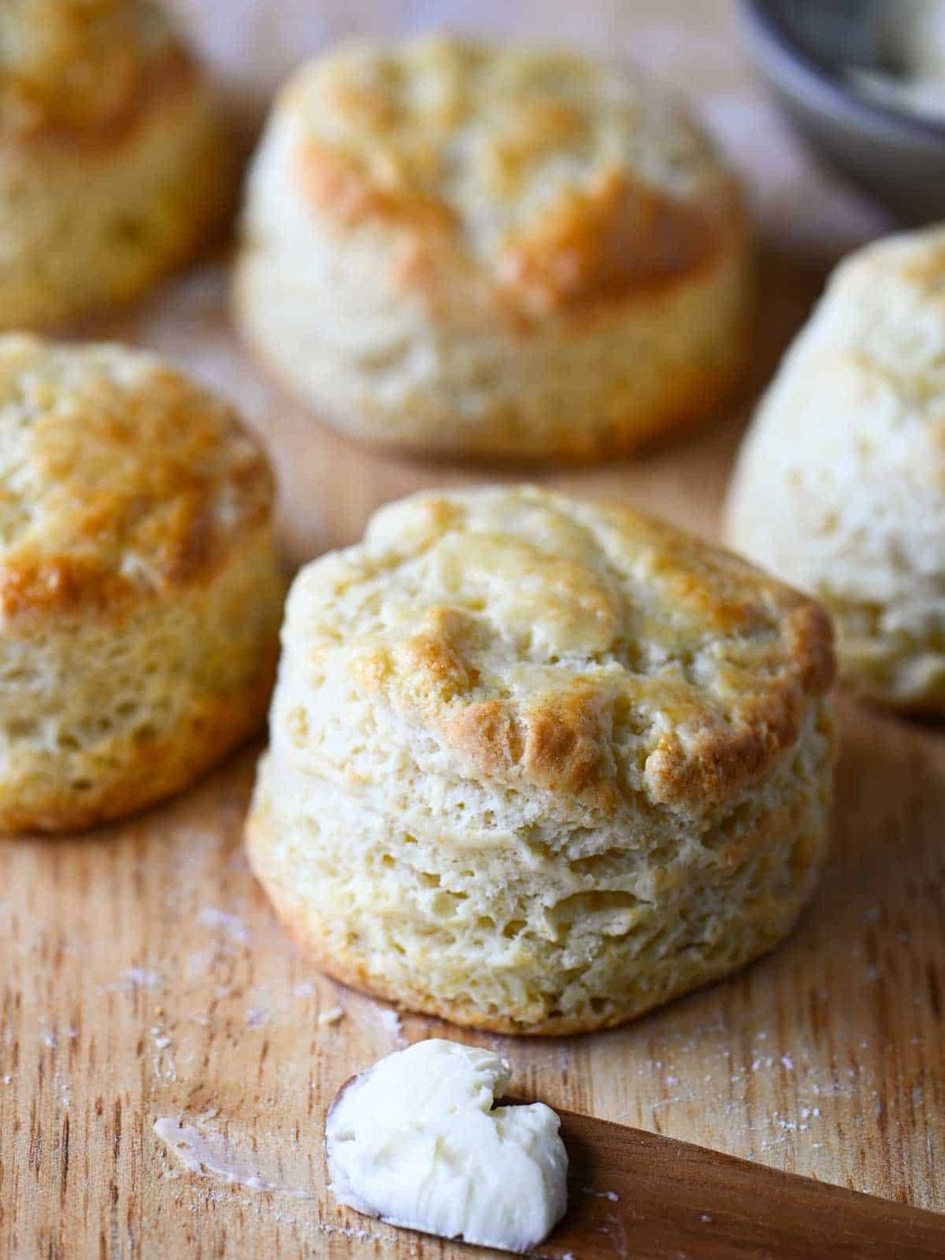 Golden biscuits on a cutting board next to a knife with butter on it.